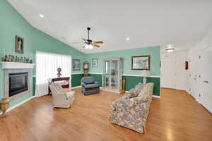 Living room with ceiling fan, lofted ceiling, a fireplace, and light hardwood / wood-style flooring