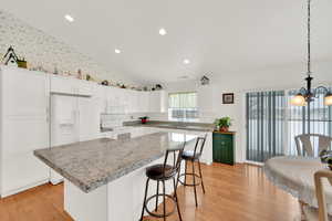 Kitchen with lofted ceiling, white appliances, white cabinetry, hanging light fixtures, and a kitchen island