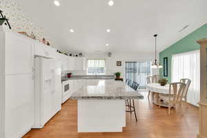 Kitchen with white appliances, lofted ceiling, a center island, and white cabinets