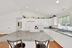 Kitchen with lofted ceiling, sink, white cabinetry, light stone counters, and white appliances