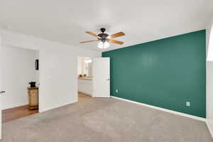 Unfurnished bedroom with connected bathroom, light colored carpet, and ceiling fan