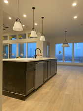 Kitchen featuring decorative light fixtures, sink, stainless steel dishwasher, a center island with sink, and light hardwood / wood-style flooring