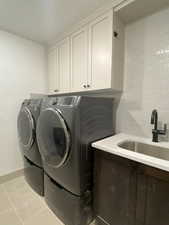 Clothes washing area featuring cabinets, separate washer and dryer, sink, and light tile patterned floors