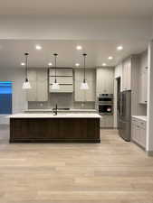 Kitchen featuring light hardwood / wood-style flooring, gray cabinetry, stainless steel appliances, a center island with sink, and decorative light fixtures