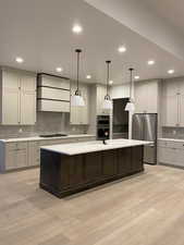 Kitchen with stainless steel appliances, a kitchen island with sink, pendant lighting, and wall chimney exhaust hood