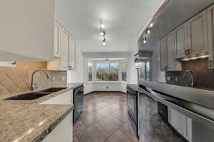 Kitchen with sink, dark tile patterned flooring, light stone countertops, decorative backsplash, and black appliances