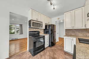 Kitchen featuring backsplash, white cabinets, light hardwood / wood-style flooring, and black appliances