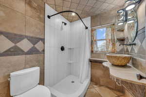 Bathroom with a shower with shower curtain, toilet, sink, and tile walls