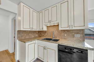 Kitchen with light stone counters, sink, decorative backsplash, and dishwasher