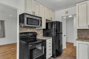 Kitchen featuring light wood-type flooring, backsplash, light stone counters, and black appliances