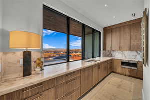Kitchen with light stone countertops, backsplash, modern cabinets, and brown cabinets