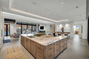 Kitchen with a tray ceiling, modern cabinets, open floor plan, a spacious island, and light stone countertops