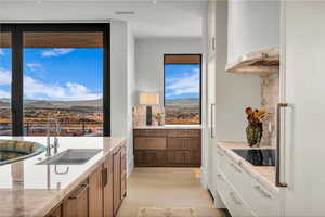 Kitchen with a mountain view, range hood, freestanding refrigerator, black electric stovetop, and white cabinetry