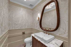 Half bathroom with vanity, ornamental molding, wallpapered walls, and wainscoting
