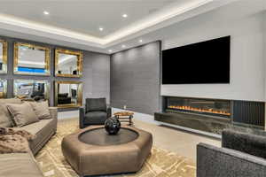 Living area featuring a glass covered fireplace, recessed lighting, a tray ceiling, and light tile patterned floors