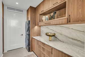Washroom with light tile patterned flooring, stacked washing machine and dryer, and cabinet space