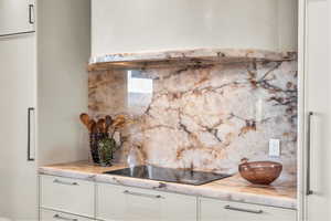 Kitchen view of backsplash, under cabinet range hood, white cabinets, and black electric cooktop