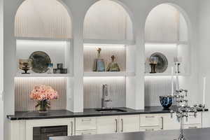 Detailed view of open shelves, wine cooler, white cabinetry, and dark stone countertops