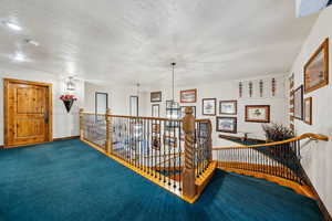 Hallway with a textured ceiling, baseboards, carpet flooring, and an upstairs landing