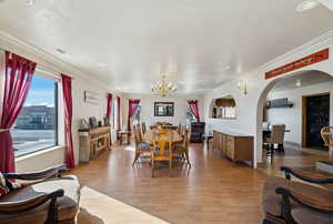Dining room with a chandelier, a textured ceiling, arched walkways, light wood-type flooring, and crown molding
