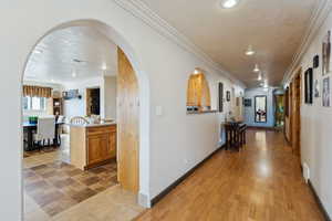 Hall featuring baseboards, arched walkways, ornamental molding, a textured ceiling, and recessed lighting