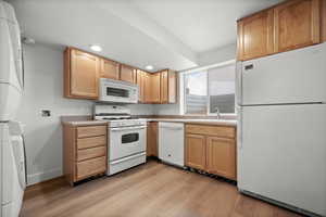 Kitchen featuring stacked washer / drying machine, sink, a textured ceiling, light wood-type flooring, and white appliances