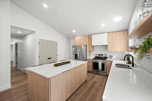 Kitchen featuring lofted ceiling, sink, stainless steel appliances, a center island, and wood-type flooring