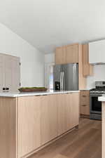 Kitchen featuring stainless steel appliances, dark hardwood / wood-style flooring, vaulted ceiling, and light brown cabinetry