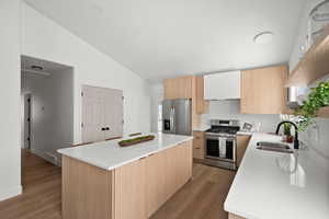 Kitchen featuring lofted ceiling, sink, appliances with stainless steel finishes, a center island, and light wood-type flooring