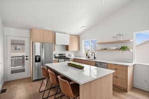 Kitchen featuring sink, a breakfast bar area, stainless steel appliances, a center island, and vaulted ceiling