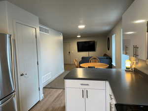 Kitchen featuring white cabinetry, light hardwood / wood-style flooring, stainless steel refrigerator, and kitchen peninsula