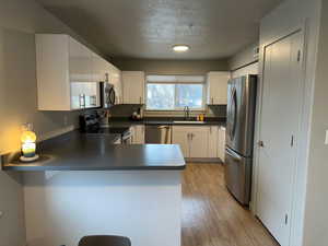 Kitchen featuring sink, white cabinetry, light hardwood / wood-style flooring, kitchen peninsula, and stainless steel appliances