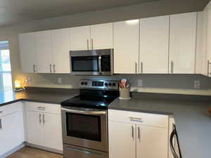 Kitchen with appliances with stainless steel finishes, light wood-type flooring, and white cabinets