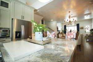 Kitchen with hanging light fixtures, a center island, light stone countertops, appliances with stainless steel finishes, and a chandelier