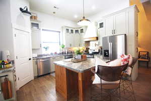 Kitchen with a center island, premium range hood, decorative light fixtures, stainless steel appliances, and wood-tile flooring