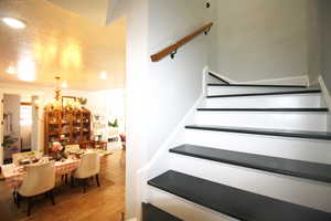 Staircase featuring a hardwood, notable chandelier, a textured ceiling, and wood-tile flooring