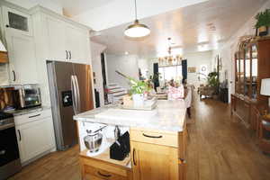 Kitchen with white cabinetry, appliances with stainless steel finishes, wood-tile flooring, and decorative light fixtures