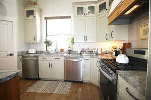 Kitchen with appliances with stainless steel finishes, light stone counters, premium range hood, wood-tile floors, and hanging light fixtures