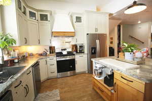 Kitchen featuring white cabinetry, wood-tile floors, premium range hood, sink, and appliances with stainless steel finishes