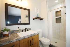 En-suite Bathroom with toilet, vanity, and a tile shower with curtain