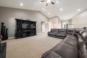 Carpeted living room with ceiling fan and high vaulted ceiling