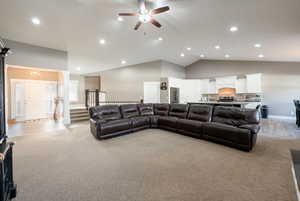 Living room with ornate columns, ceiling fan, light colored carpet, and high vaulted ceiling