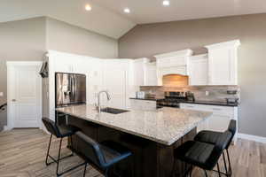 Kitchen featuring white cabinetry, stainless steel appliances, a breakfast bar, and a kitchen island with sink