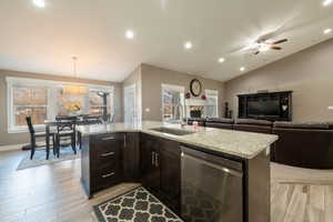 Kitchen with sink, a kitchen island with sink, decorative light fixtures, vaulted ceiling, and stainless steel dishwasher