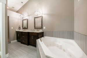 Bathroom with vanity, lofted ceiling, and tiled bath