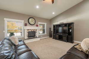 Living room with a healthy amount of sunlight, light colored carpet, lofted ceiling, and a fireplace