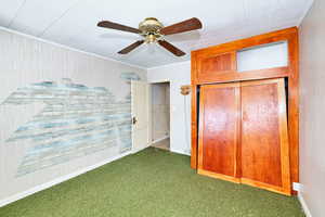 Unfurnished bedroom with wooden walls, a closet, ceiling fan, and dark colored carpet