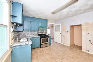 Kitchen with blue cabinets, stainless steel range with gas cooktop, sink, and decorative backsplash