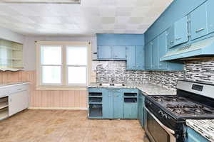 Kitchen featuring tasteful backsplash, stainless steel gas range oven, blue cabinetry, and wood walls