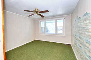 Carpeted empty room with wooden walls, ornamental molding, and ceiling fan